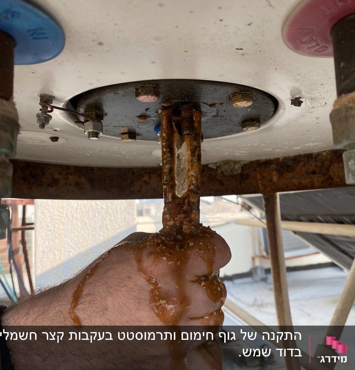 יד אוחזת בצינור דודי שמש עם חלודה ונזילה